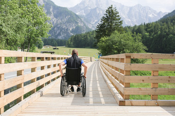Disabled young man on a wheelchair on a wooden bridge path enjoying in nature