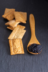 Top view of toasted muffins with caviar on wooden spoon with slate background in vertical with copy space