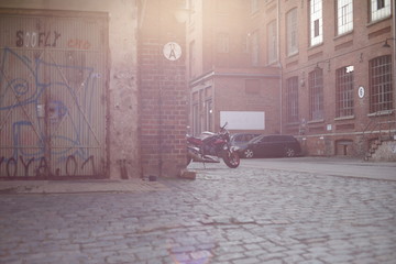 cobblestone paved court of an old industrial area with brick wall buildings in bright sunlight -...