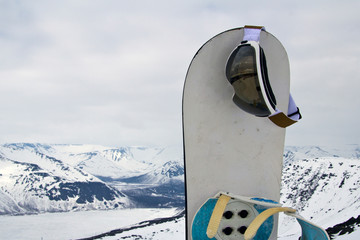 a snowboard stuck in the snow and ski goggles hanging on it. Concept to illustrate ski admission fee.
