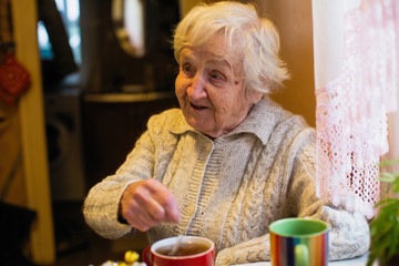Elderly woman, drinking tea sitting at the table in the house. Grandmother.