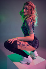 Young fitness blonde woman wearing blue velour booty shorts posing on camera, making squats on top...