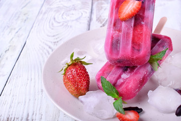 Berry popsicles with pieces of strawberry and honeysuckle on the white plate