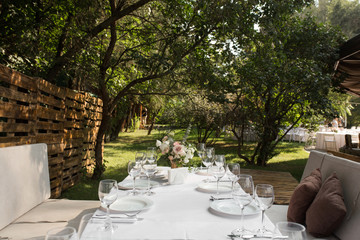 Wedding table setting decorated with fresh flowers in a brass vase. Wedding floristry. Banquet table for guests outdoors with a view of green nature. Bouquet with roses, eustoma and eucalyptus leaves