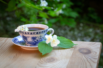 Beautiful cup of coffee on a background of green with flowers. Wooden table. Jasmine flowers. Pleasant breakfast. Summer sunny day.