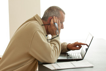 Casual dressed man pointing at computer screen and holding a pair of lasses in right hand. Papers...