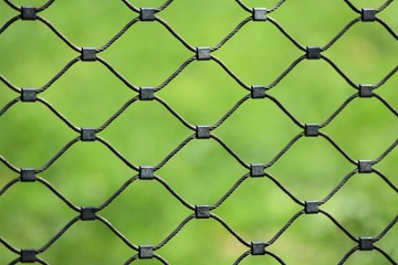 Close-up of a wire fence with blurred green grass background