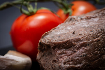 Grass Fed Corn Roast Beef garnished with Tomatoes and Garlic on natural black stone background.