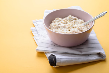 Pink plate with oatmeal is on a towel on a yellow background