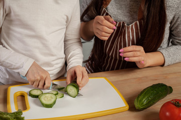 Mother and her daughter are making a vegetable salad and having fun at the kitchen.