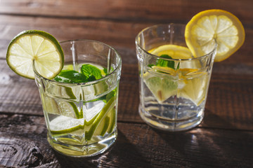 Two glasses of water, lemon, mint and ice on a wooden table