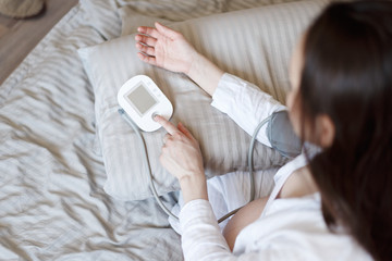 Top view of brunette woman in bed measuring blood pressure
