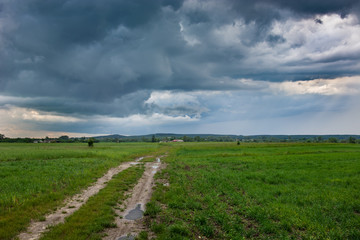 Dirt road through the field and storm clouds in the sky