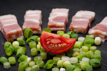 Uncured Apple Smoked Bacon, Red Tomatoes and Green Onion Scallions  arranged on black natural stone background.