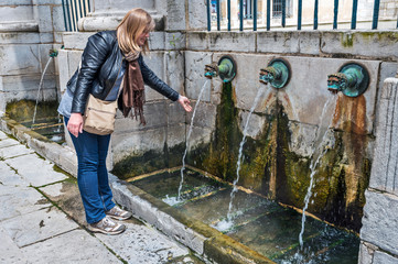 Women is touching the hot water jet from the thermal source in the center of Dax city. Southwestern...