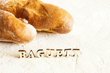 Baguette on a light background. The inscription "bakery" in wooden letters on a textural background. Place for text.