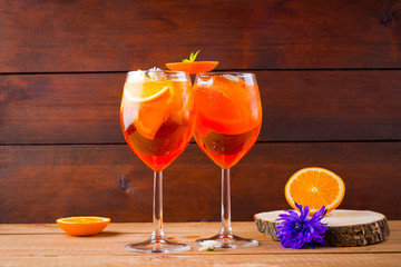 Cocktail aperol spritz on wooden boards. Summer alcoholic cocktail with orange slices and flowers. Aperol spritz on wooden boards