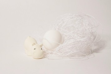 white toy hippo with an egg and a nest on white background