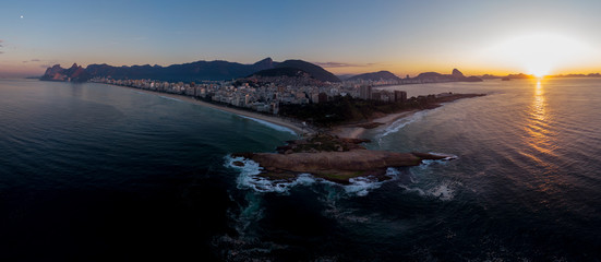 Aerial wide panorama of Rio de Janeiro with Arpoador cliff and wider cityscape and skyline in the background against a colourful sunrise sky
