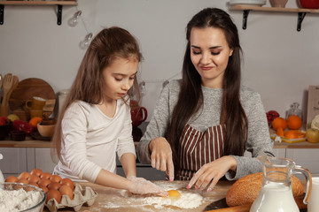 Mother and her daughter are baking a bread and having fun at the kitchen.