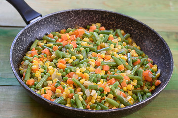 Frying pan with roasted vegetables on rustic wood green background.Green peas, carrot, corn , green beans, onion in the wok.Healthy food concept.