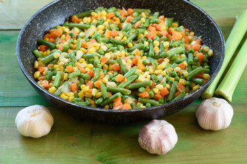 Fresh, healthy celery, garlic heads and mix on vegetables fried in a wok on wooden rustic background. Green peas, carrot, corn , green beans, onion in the pan.Copy space.