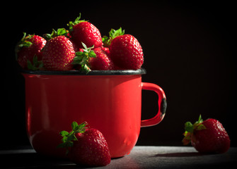 Fresh Strawberries in red enamel cup on black  background