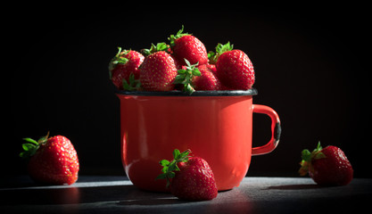 Fresh Strawberries in red enamel cup on black  background