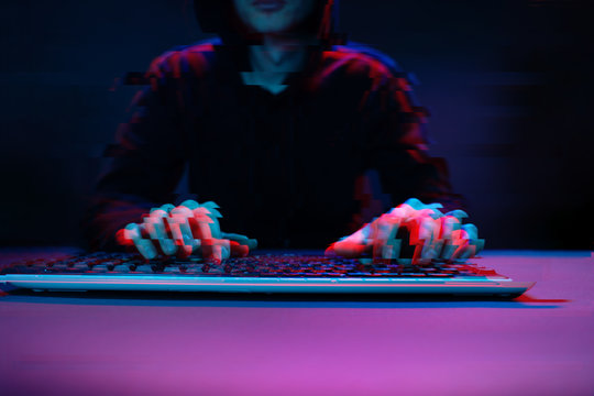 Hacker in the hood working with computer typing text in dark room. Image with glitch effect