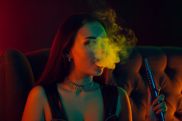 Sexy brunette model is smoking a hookah exhaling a smoke at a luxury night club.