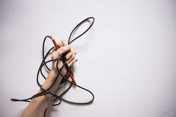 Close-up of hand holding a red pen with a black wire around them on a white background with copy space – Cable warped over person’s arm and writing tool
