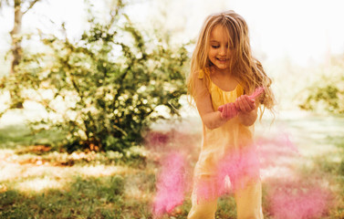 Obraz na płótnie Canvas Adorable little girl playing in the park with magical pink dust for an imagination or fairy tale concept. Happy child smiling broadly and playing with pink powder during her birthday party in the park