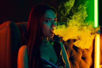 Sexy brunette model is smoking a hookah exhaling a smoke at a luxury night club.