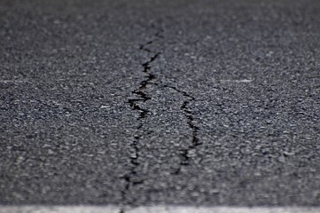 An image of gray asphalt road split by a crack. A metaphor concept for an age crisis, broken dreams, psychological break, marriage relationship problems, shattered trust