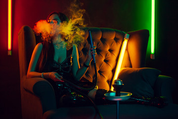 Sexy brunette model is smoking a hookah exhaling a smoke at a luxury night club.