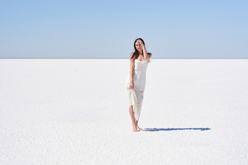 Dark-haired girl in a white dress posing on the dried up salt lake Elton in the Volgograd region in Russia.