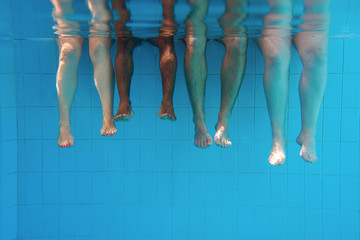 four people legs underwater in the swimming pool. Friends. Party. Summer. Vacation and sport...