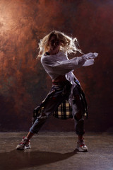 Fototapeta na wymiar Photo of young dancing blonde woman in ripped jeans and sneakers on dark brown background