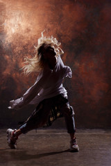 Fototapeta na wymiar Photo of slim blonde dancer woman in torn jeans and sneakers on a dark brown background