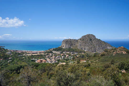 Landscape of historic italian city Cefalu in the island Sicily with ruined mediaeval fortress or castle on the top of the mountain which protected city agains pirate raids and blue sea in background.