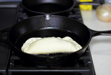 Pan fried calzone cooking in a cast iron skillet on a stove.