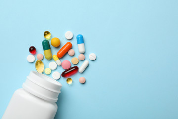 Bottle and scattered pills on color background, top view. Space for text