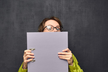 Portrait of afraid girl looking out from big folder