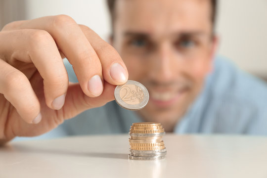 Young smiling man stacking coins at table, focus on hand