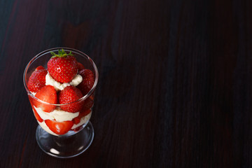 Whipped cream and strawberries served in a glass. Dark wooden table, high resolution