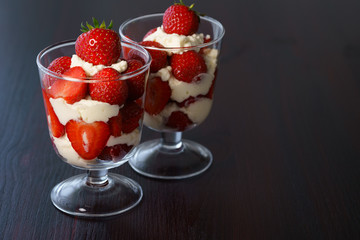 Whipped cream and strawberries served in a glass. Dark wooden table, high resolution