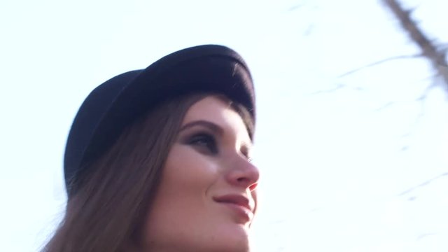 Close-up of beautiful young woman in a dark hat and black leather jacket with stylish makeup looking at camera in spring summer day. Action. Urban modern stylet