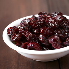 Dried cranberries in small bowl, photographed on dark wood with natural light (Selective Focus, Focus on the cranberries on the top)