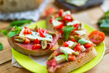 Traditional Italian bruschetta with blue cheese, feta, tomatoes, basil leaves, jamon on a wooden background.