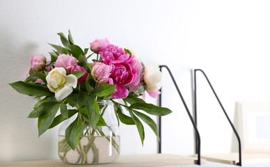 Shelf with vase of beautiful peonies on white wall. Space for text